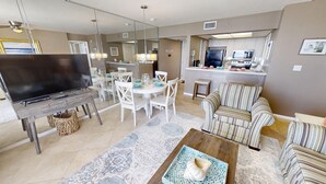 Un salon moderne comprenant un téléviseur, un coin repas, une cuisine et un canapé à rayures.