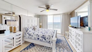 Une chambre spacieuse avec un grand lit, un ventilateur de plafond, une télévision et une vue sur l’océan.
