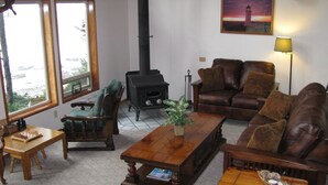 Uma sala de estar acolhedora com lareira, sofá de couro, mesa de centro de madeira e vista para o exterior.