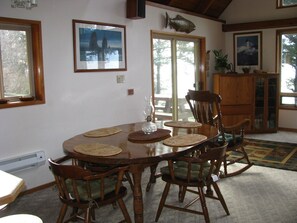 Une salle à manger avec une table ronde en bois, six chaises en bois dotées d’assises rembourrées et un motif décoratif représentant un poisson sur le mur.