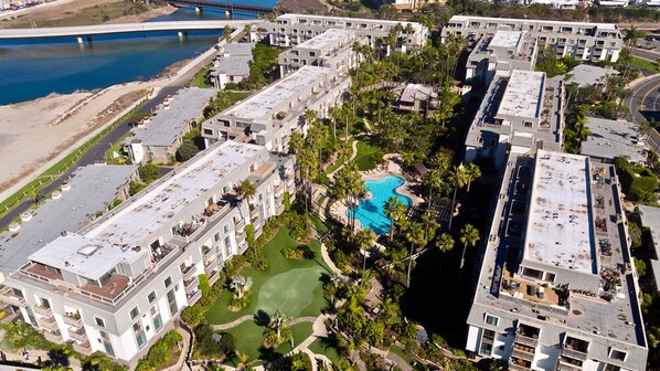 A high-rise hotel with multiple balconies, a central swimming pool, and a view of a river.