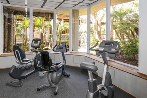 A gym with three stationary bikes, large windows, and a view of greenery outside.