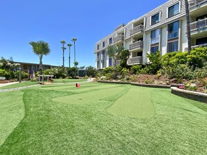 A well-maintained courtyard with a putting green, surrounded by multi-story buildings with balconies and a clear blue sky.
