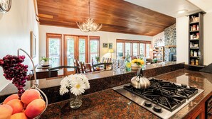 A kitchen with granite countertops, a gas stove, wooden ceiling, and a stone backsplash.