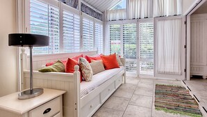 A cozy room with a white bench, a lamp, and a view through large windows with shutters. - Pet Friendly ~ Golf Cart~ Private Patio (Destin)