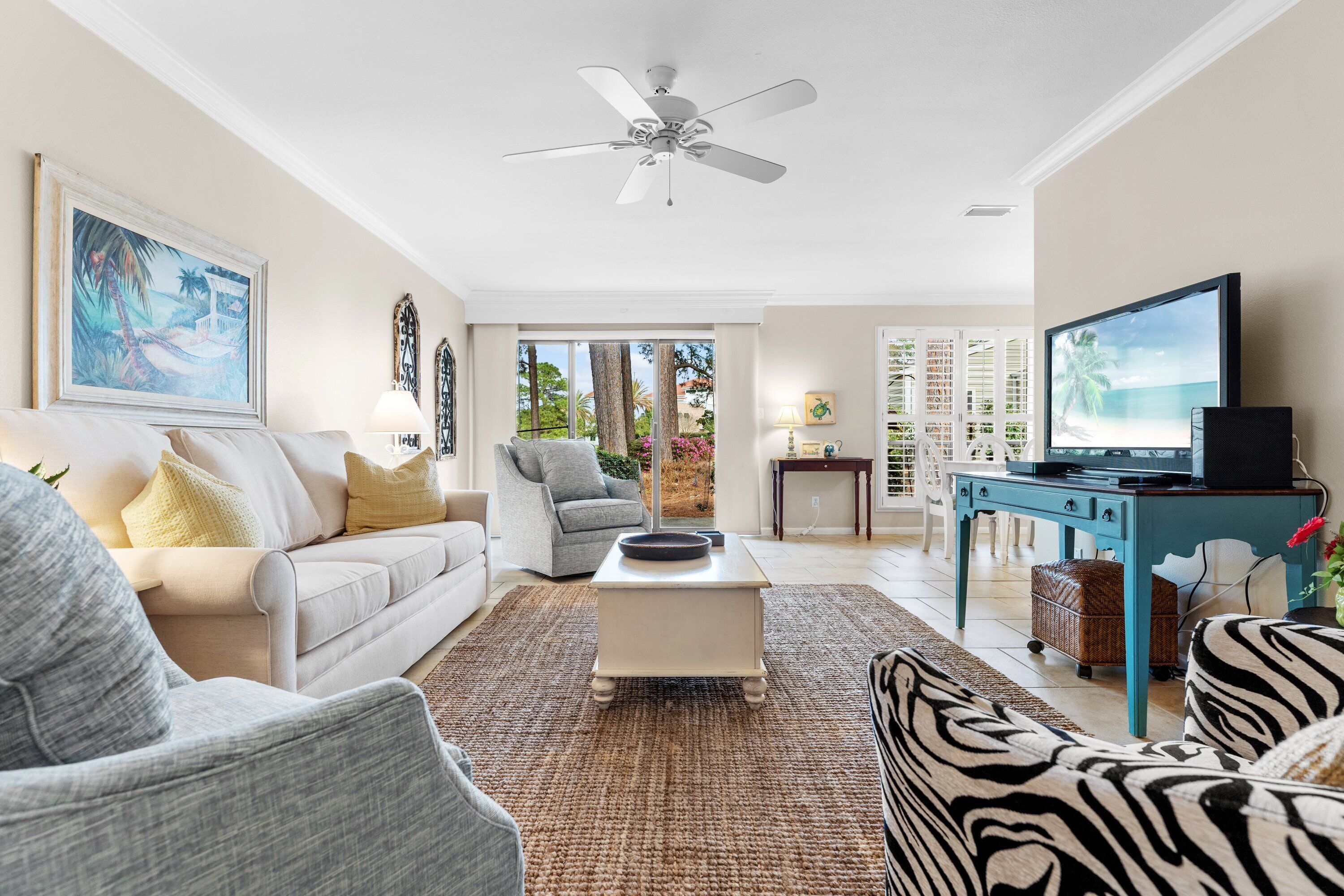 A spacious living room with a white sofa, a grey armchair, a zebra-patterned sofa, a coffee table, and a television on a blue stand.