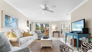 A spacious living room with a white sofa, a grey armchair, a zebra-patterned sofa, a coffee table, and a television on a blue stand. - Pet Friendly ~ Golf Cart~ Private Patio (Destin)