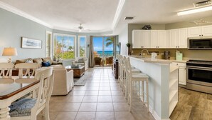 A spacious living area with a view of the ocean, a kitchen with white cabinets, and a dining area with a table and chairs. - 2403 SeaCrest-4th Floor/ Ocean Views & Newly Updated (Hilton Head Island)
