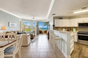 A spacious living area with a view of the ocean, a kitchen with white cabinets, and a dining area with a table and chairs.