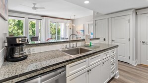 A modern kitchen with a granite countertop, stainless steel sink, and white cabinetry.