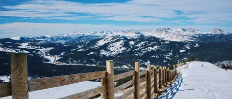 A wooden fence along a snowy mountain path with a view of snow-covered peaks in the distance.