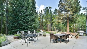 Een terras buiten met een ronde tafel en stoelen, omgeven door hoge bomen.