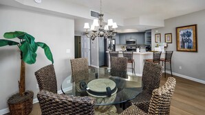 Un coin repas avec une table en verre entourée de chaises en osier, un lustre et une plante en pot.