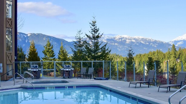En swimmingpool med utsikt över snöklädda berg, utomhusgrillar och solstolar.