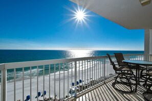A balcony with a view of the beach and ocean, featuring a table and chairs.