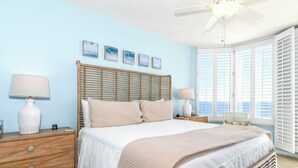 Un dormitorio con cama, cabecero de madera, mesitas de noche y lámparas, con vistas al exterior.