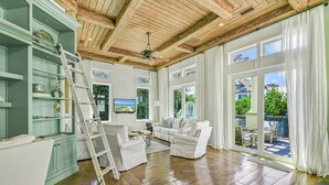 A spacious living room with a wooden ceiling, large windows, and a view of the outdoors.