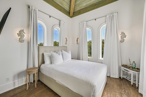 A bedroom with a large bed, white curtains, and decorative seahorse wall art.