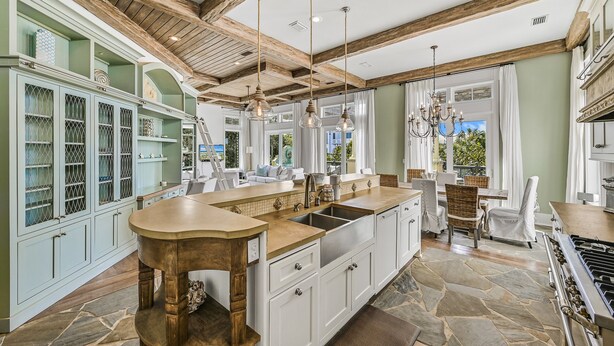 A spacious kitchen with a large island, wooden beams, and a stone floor.