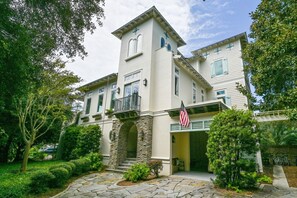 A two-story building with a stone archway entrance, a balcony with an American flag, and a covered porch area. - Gulf Views & Private Pool Just 105 Feet From Beach Access- 30A Mojo (Santa Rosa Beach)