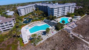A resort with multiple swimming pools, a large building with balconies, and a landscaped area with palm trees. - 1106 SeaCrest-Oceanviews, walk to dining, shopping & activities. (Hilton Head Island)