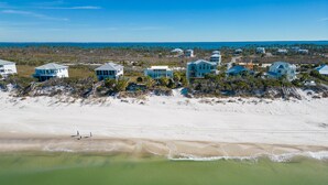 An aerial view of a coastal area with multiple beachfront properties, including houses and villas, and a sandy beach with gentle waves. - Magnolia: 7 BR Beachfront Home - Pet Friendly, Priv. Pool, Sleeps 24! (Cape San Blas)
