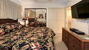 A bedroom with a large bed, a dresser, a television, and a ceiling fan. - Unwind by the Waves: Kihei Beach #203, Prime Beachfront Tropical Escape! (Kihei, Maui)