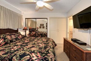 Ein Schlafzimmer mit einem großen Bett, einem Schminktisch, einem Fernseher und einem Deckenventilator.
