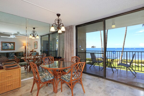A dining area with wicker chairs and a glass table, a ceiling fan, and a view of the ocean through large glass doors.