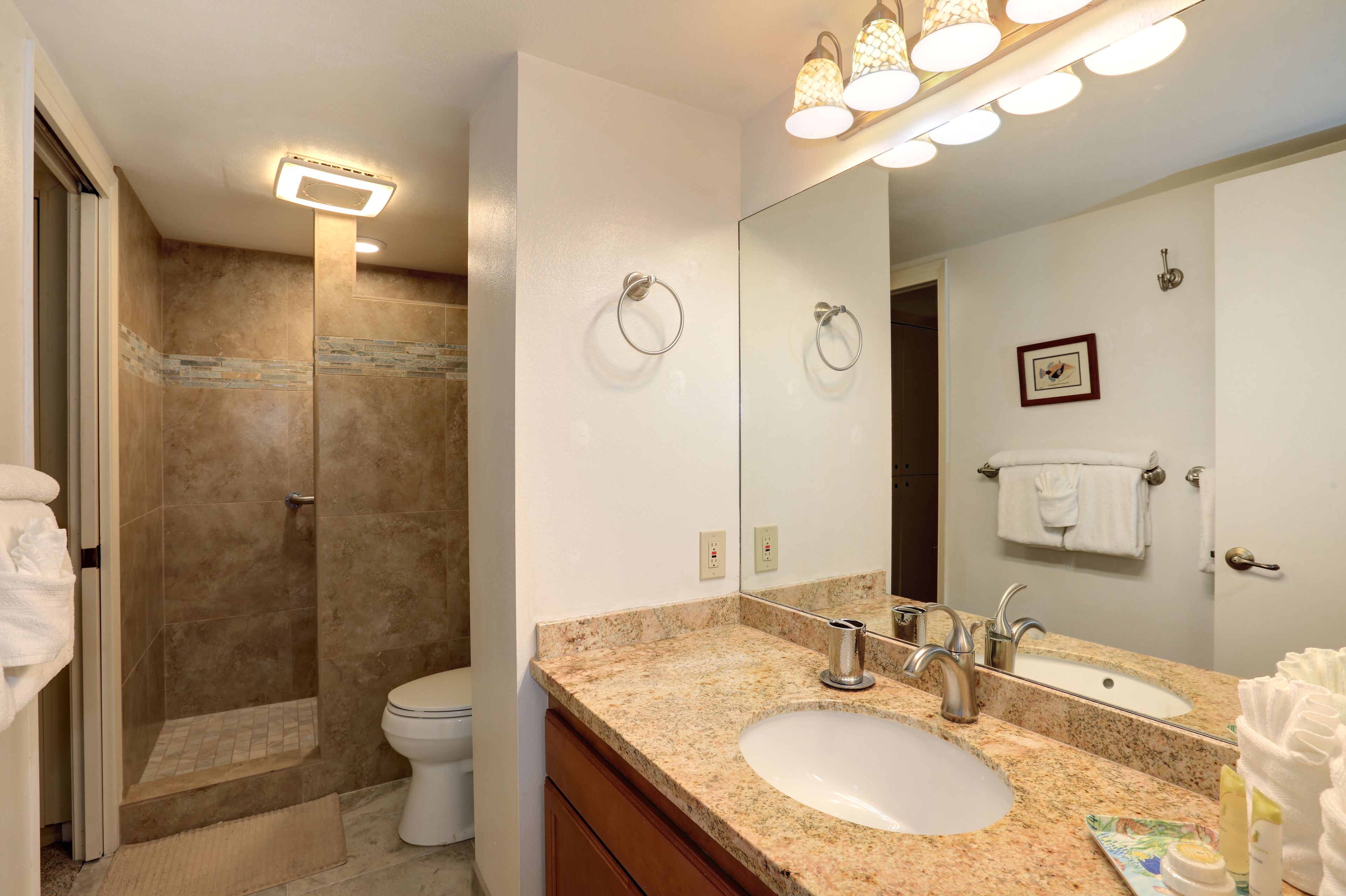 A bathroom with a shower, toilet, sink, and a large mirror.