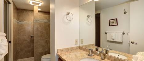 A bathroom with a shower, toilet, sink, and a large mirror.