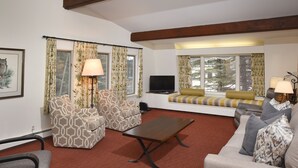 Una sala de estar con sillones estampados, un sofá, una mesa de centro y un televisor.