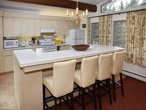 A kitchen with a central island, white cabinets, a microwave, a stove, and a refrigerator. There are four chairs around the island and a chandelier above.
