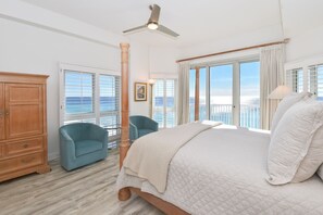 Relax in this serene bedroom with a large bed, ceiling fan, and ocean views from the balcony.