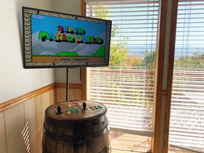 A television displaying 'Super Mario World' with a wooden barrel and blinds in the background. - Cabin w/Amazing Mountain Views-Hot Tub-Game Room (GATLINBURG)