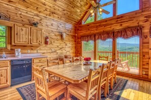 A wooden cabin with a kitchen featuring wooden cabinets, a dining table with chairs, a ceiling fan, and large windows with blinds. - Cabin w/Amazing Mountain Views-Hot Tub-Game Room (GATLINBURG)