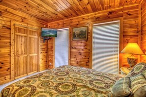 A wooden cabin bedroom with a bed, a television, and a window with blinds. - Cabin w/Amazing Mountain Views-Hot Tub-Game Room (GATLINBURG)