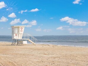 Une tour de surveillance, où se tient un sauveteur, sur une plage de sable, avec un ciel dégagé.