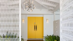 A bright yellow door with a modern chandelier above, white walls, and decorative metal fencing. - Regency Modern - Indian Canyons Hollywood Regency! (Palm Springs)
