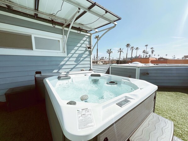 A hot tub with a label indicating 176 watts and a 50-gallon capacity, located outdoors with a view of palm trees and a clear sky.