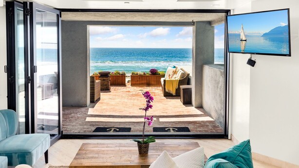 Ein modernes Wohnzimmer mit einem großen Schiebeglasfenster, das auf eine Terrasse im Freien mit Meerblick führt.