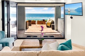 A modern living room with a large sliding glass door leading to an outdoor patio with a view of the ocean.