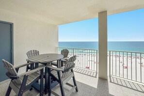 A balcony with a table and chairs, a view of the beach, and a door.