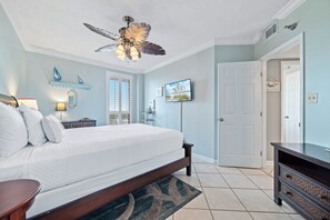A bedroom with a bed, a ceiling fan, a TV, and a door.