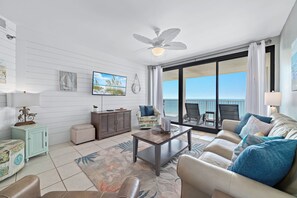 A spacious living room with a ceiling fan, a large window with a view, a sofa, a coffee table, and a side table.