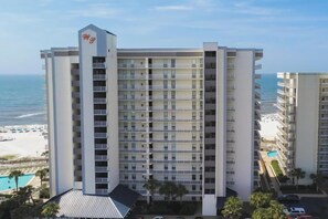 A multi-story hotel with balconies, a pool, and a beach view.
