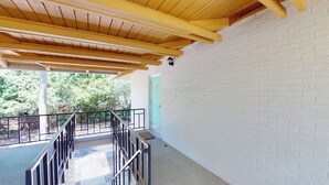 Un espacio al aire libre techado, con techo de madera, paredes de ladrillo blanco y baranda de metal.