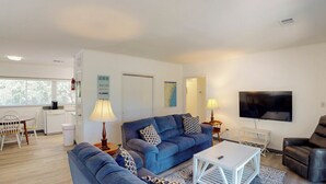 Una sala de estar moderna con un sofá azul, una mesa de centro, un televisor y un comedor con una mesa y sillas.