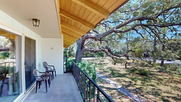 Un espacio exterior techado con techo de madera, una puerta de cristal que da a una habitación y un gran árbol al fondo.