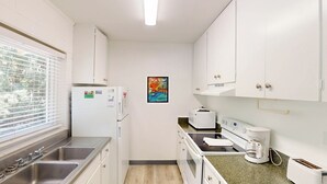 Cocina compacta con gabinetes blancos, refrigerador, microondas, cafetera y tostadora.
